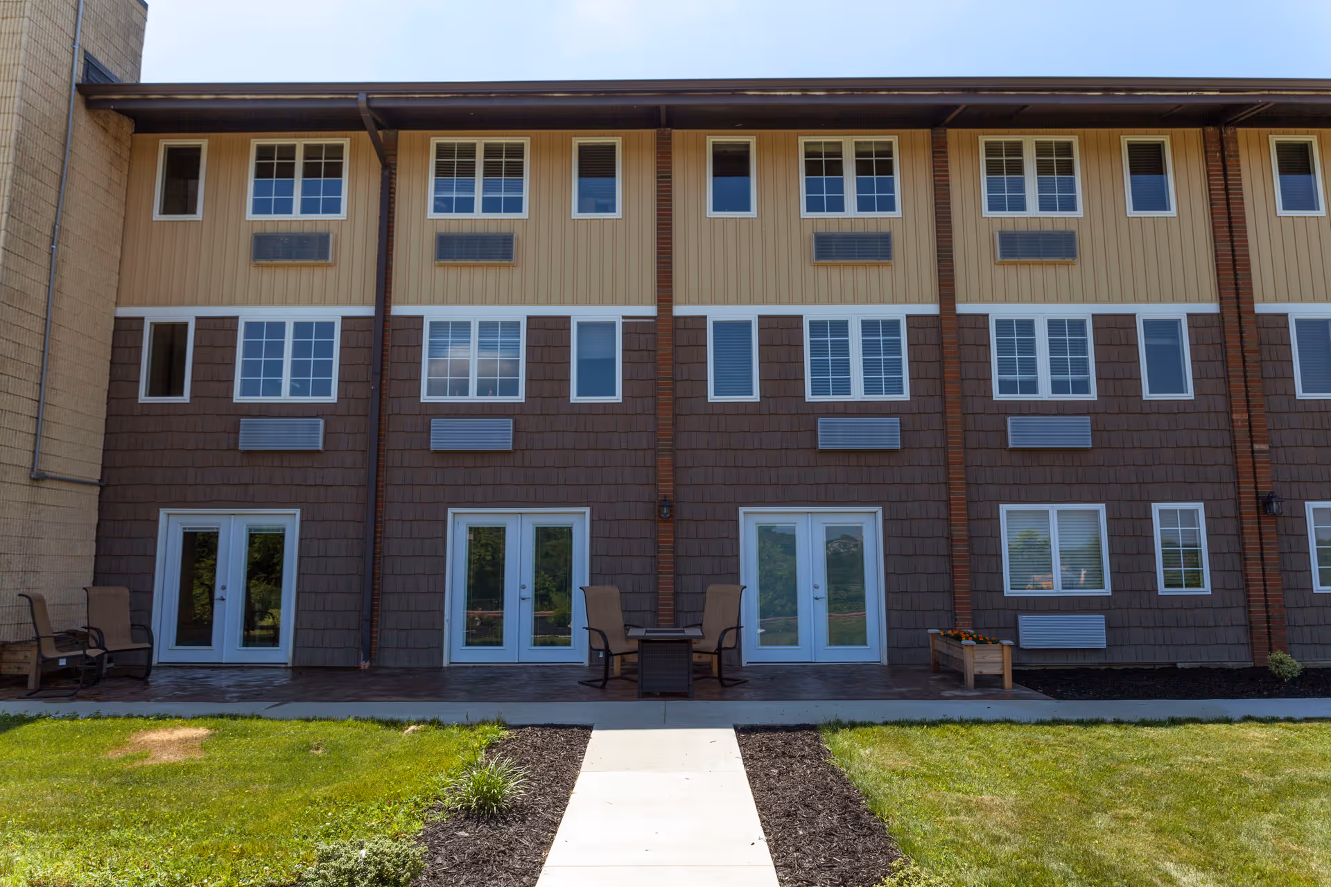 Three-story Walden's View Senior Living exterior with ground-floor patios and seating.