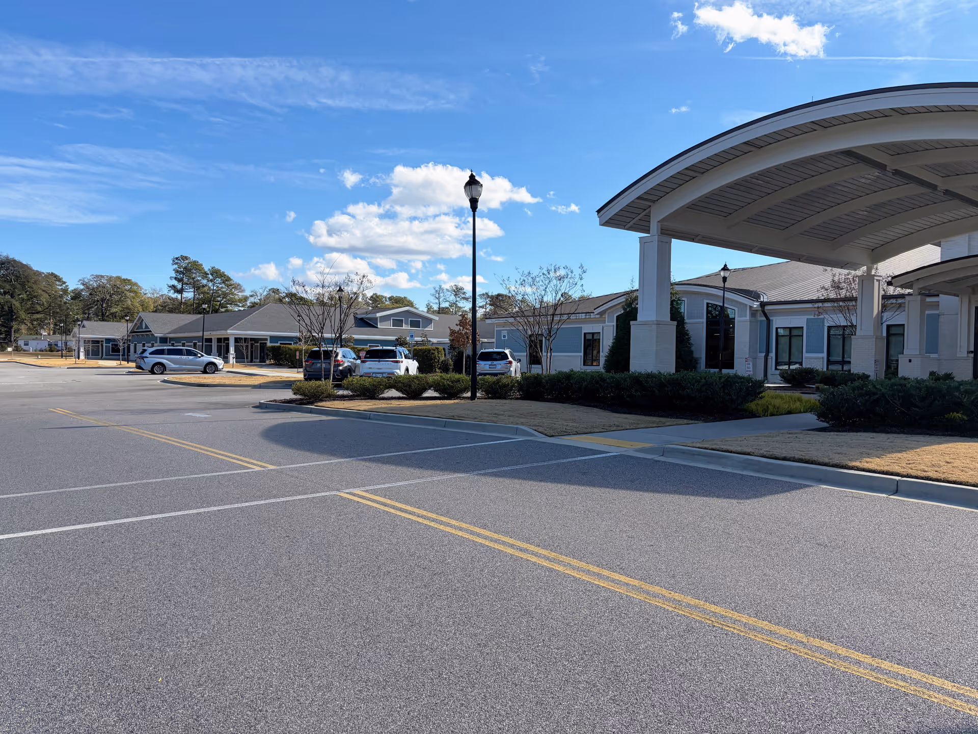 Senior living facility exterior with covered entrance, parking lot, and landscaping.