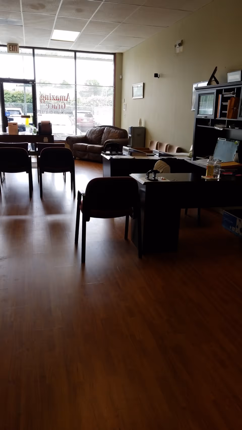 Empty reception area with desks, chairs, and a leather sofa by large glass doors.