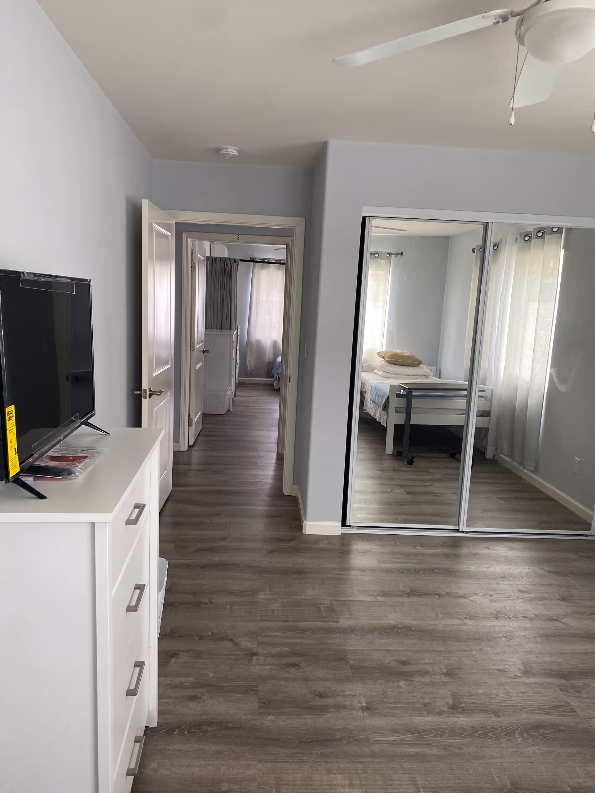 Modern senior living apartment hallway with dresser, TV, and mirrored closet.