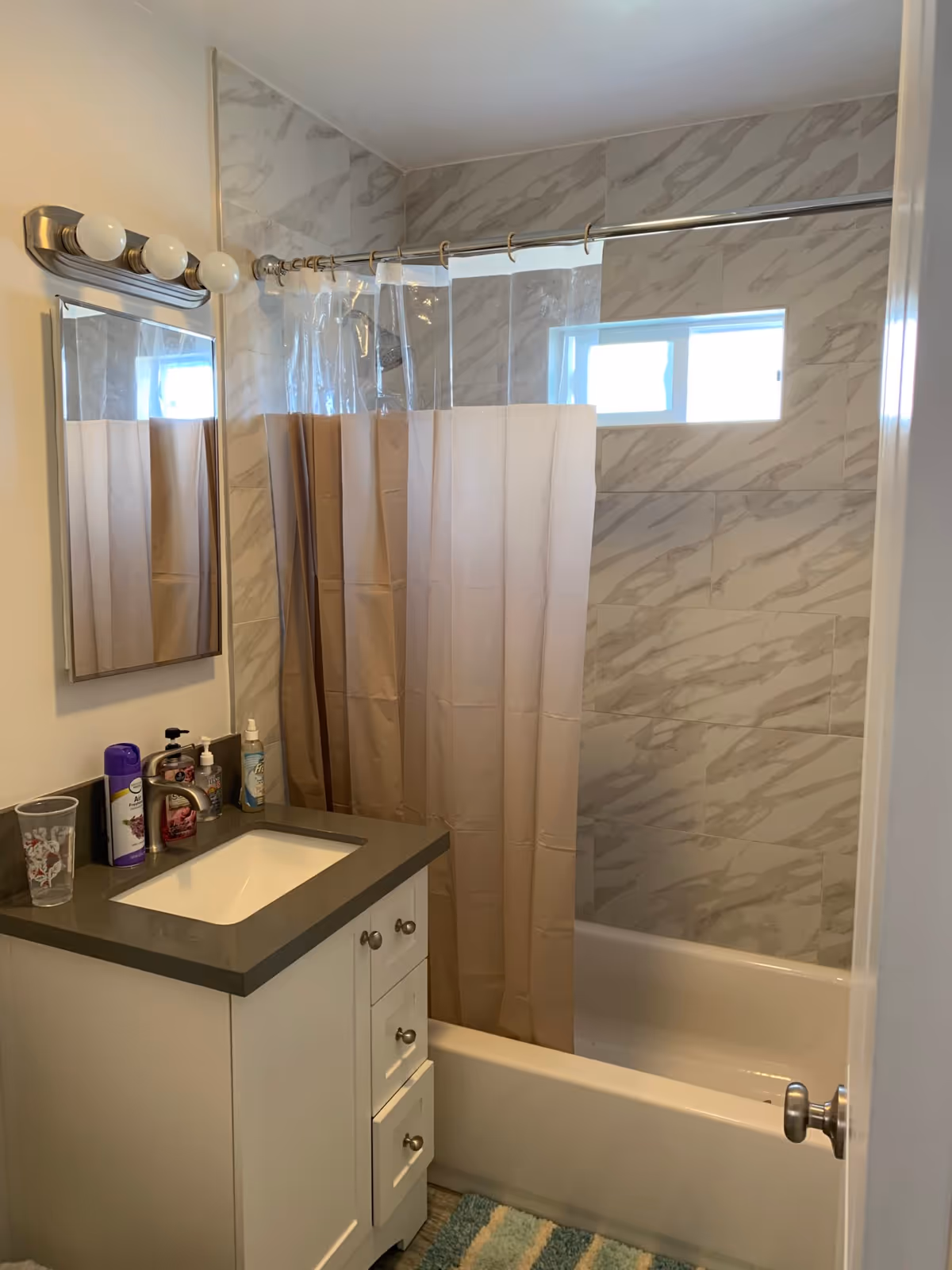 Bathroom with a white vanity, mirror, shower curtain, and marble-tiled shower area.