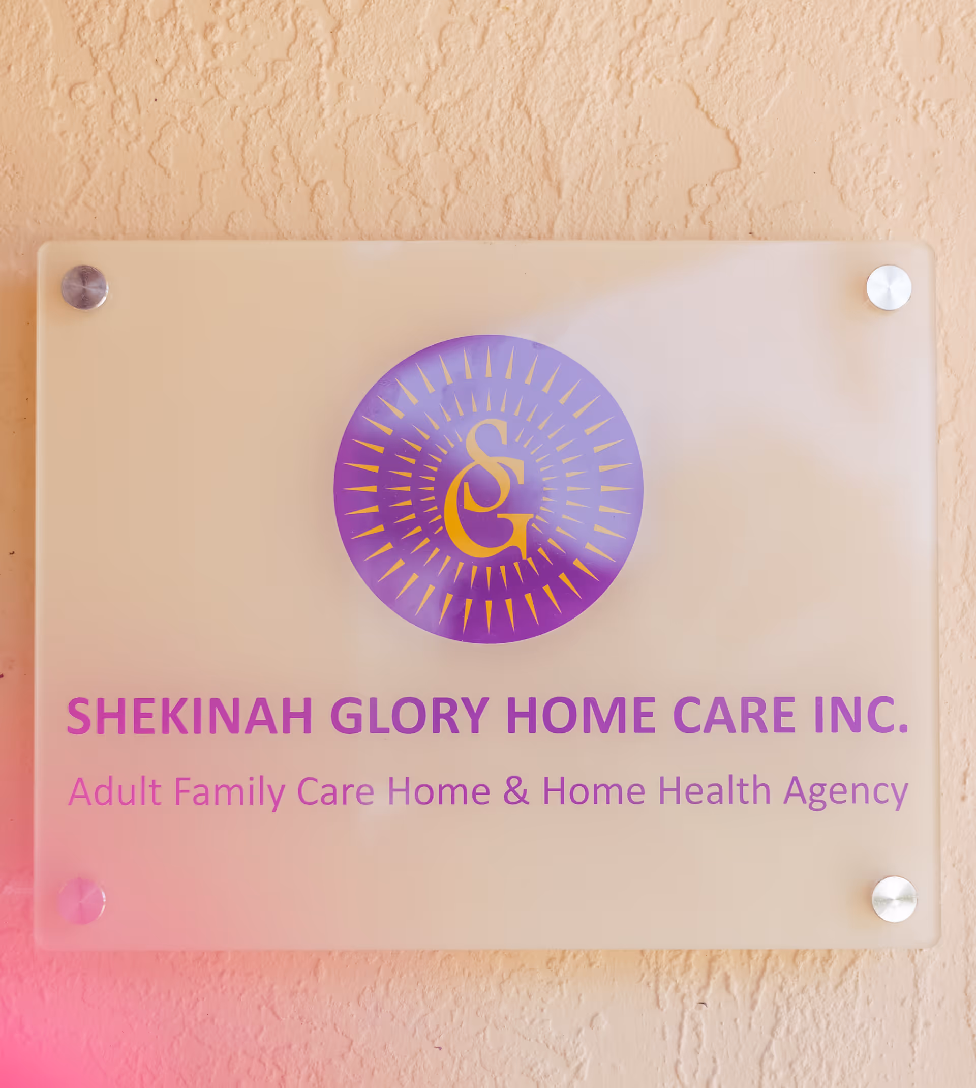 Frosted glass plaque with purple logo and Shekinah Glory Home Care text on a wall