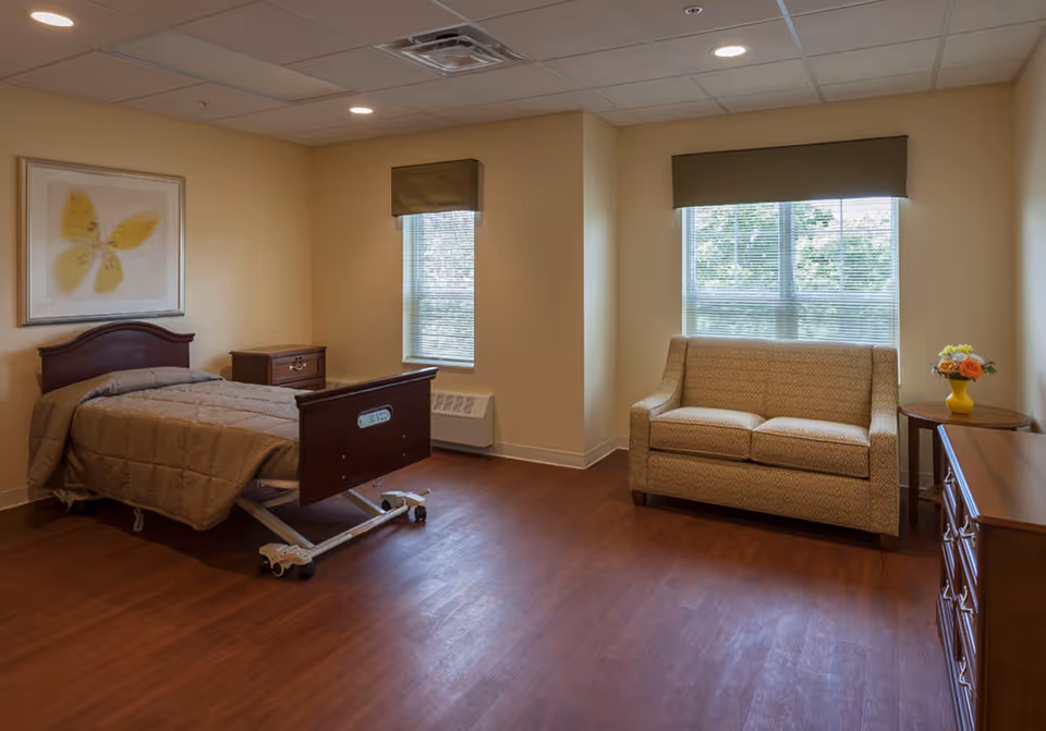 A spacious senior living bedroom with a hospital-style adjustable bed, sofa, and wooden furniture.