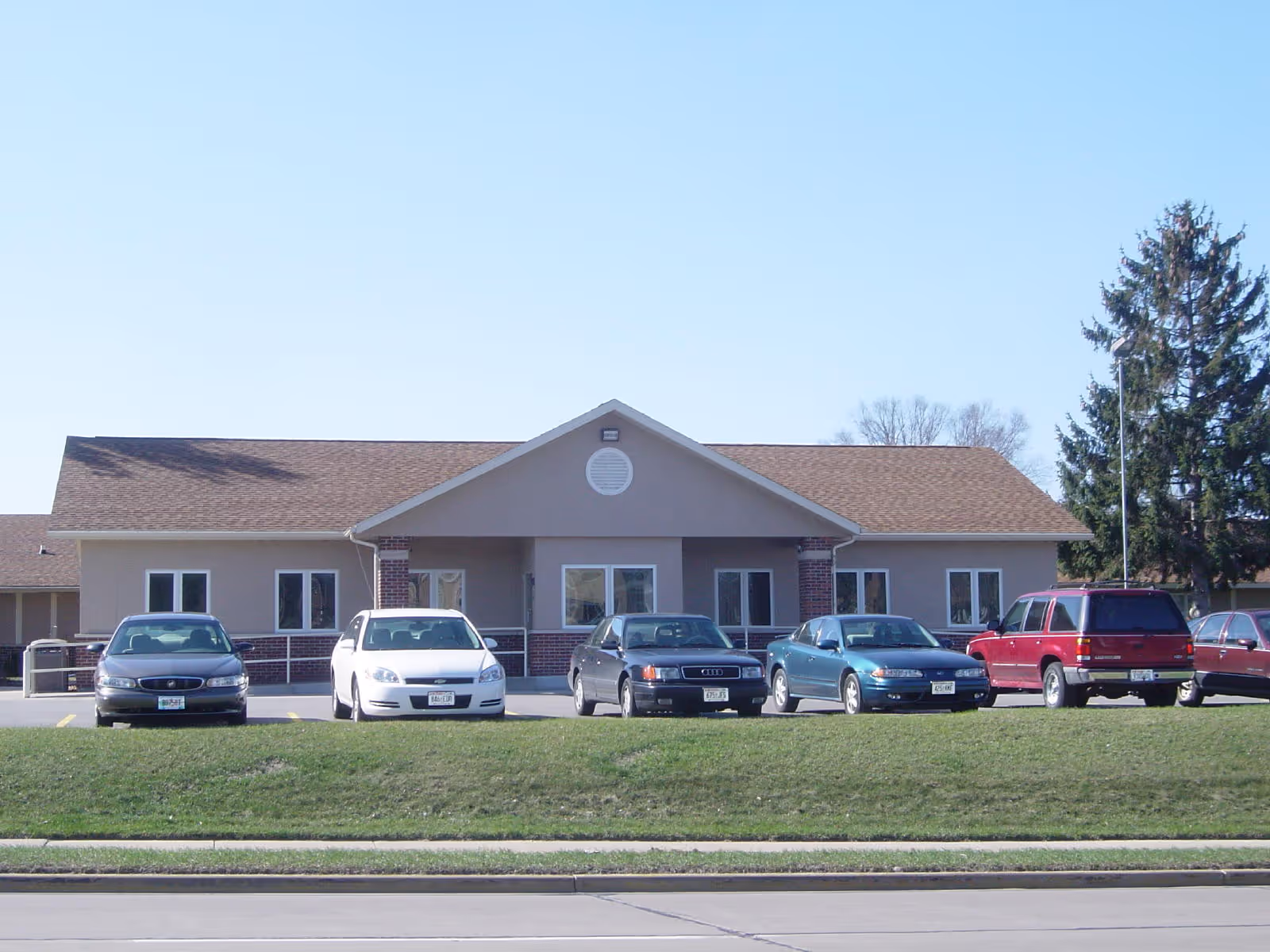 Single-story senior living center with a gabled roof and cars parked in front.