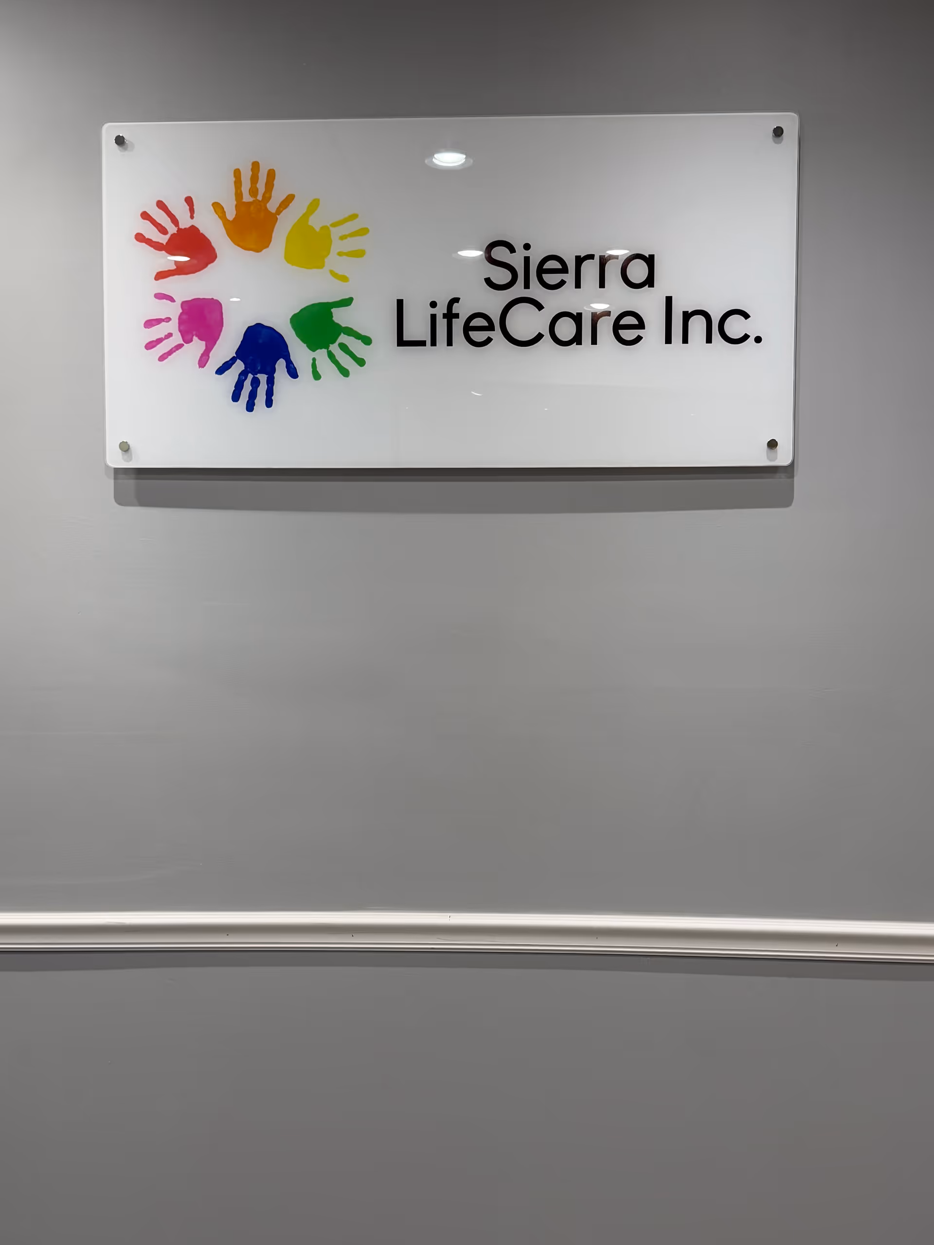 White sign with colorful handprints and Sierra LifeCare Inc. on a gray wall.