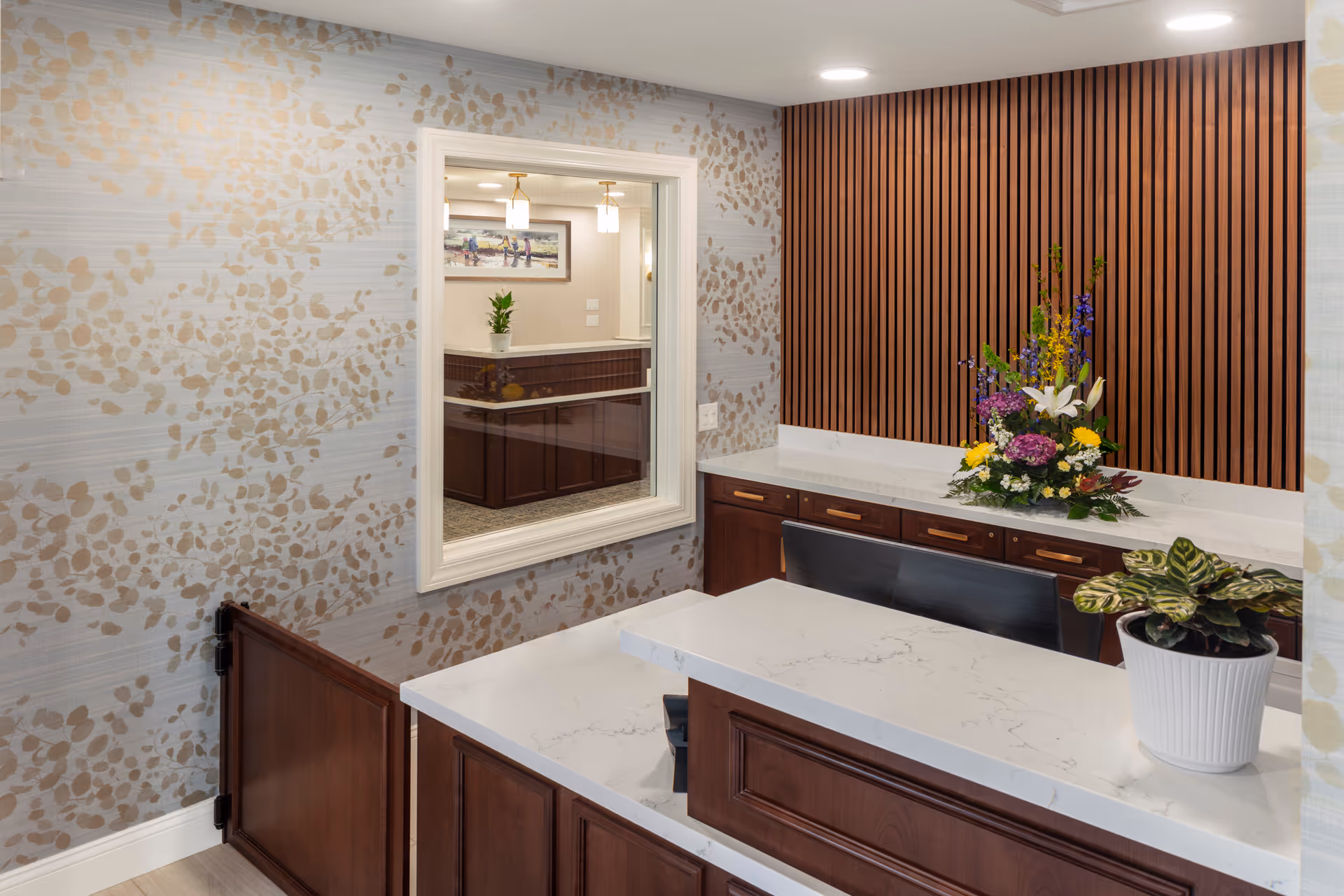 Interior reception area with marble countertop, wooden panels, flowers, and a windowed service desk.