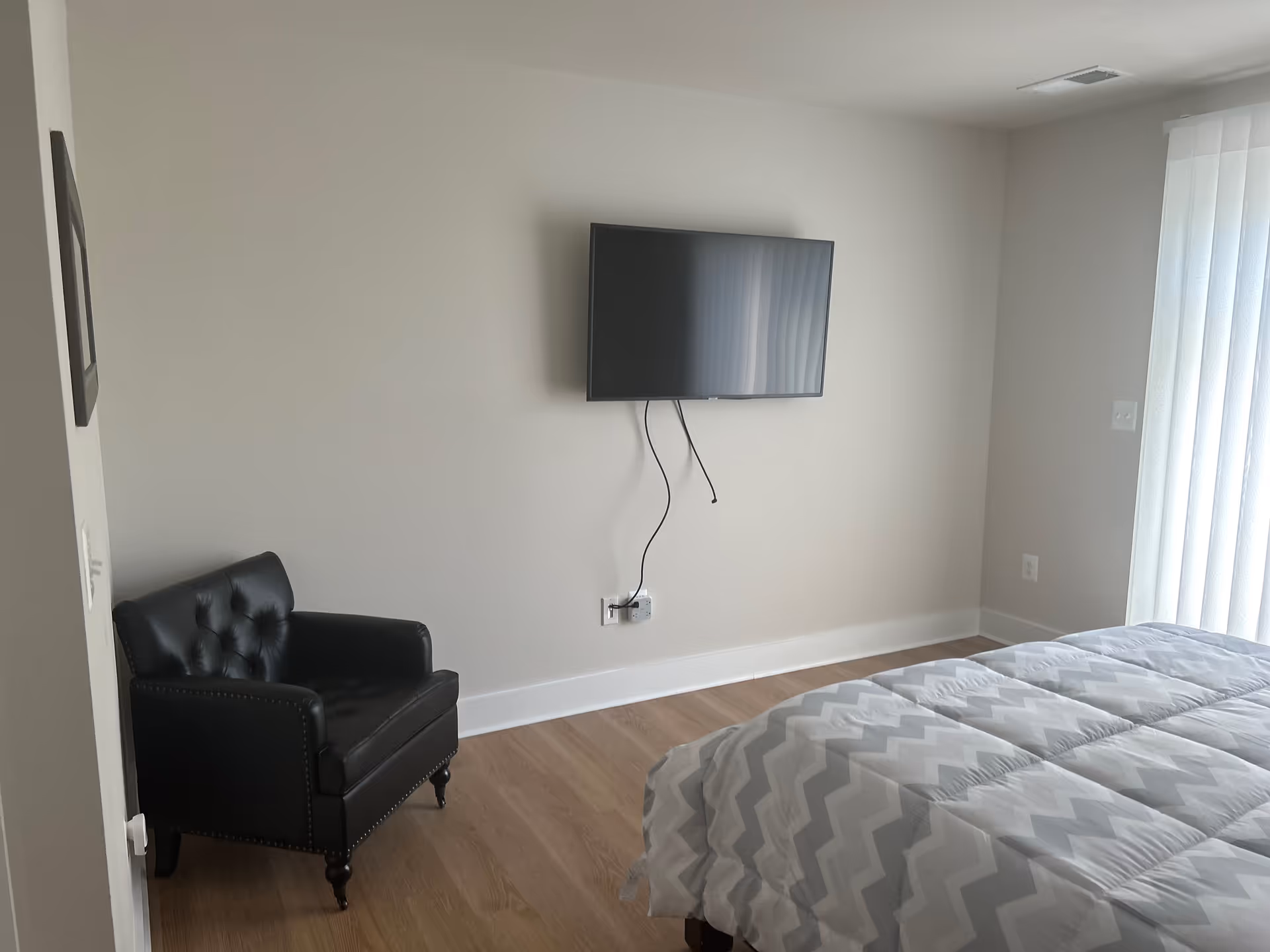 Bedroom with wall-mounted TV, black leather chair, and bed with chevron bedding.