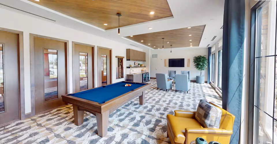 Bright modern lounge with pool table, seating, kitchenette, and large windows.