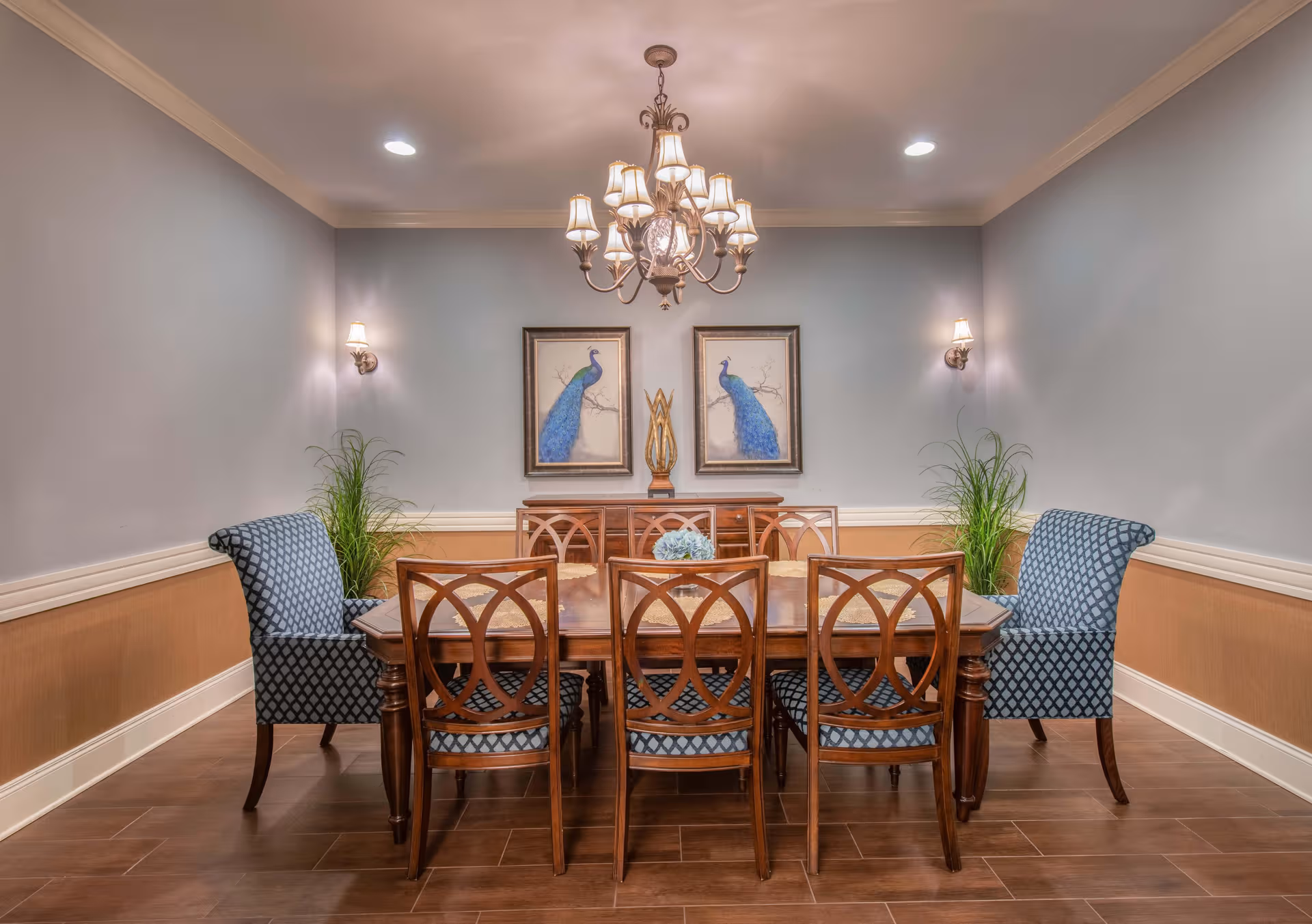 Elegant dining room with a wooden table, blue patterned chairs, chandelier, and framed wall art.