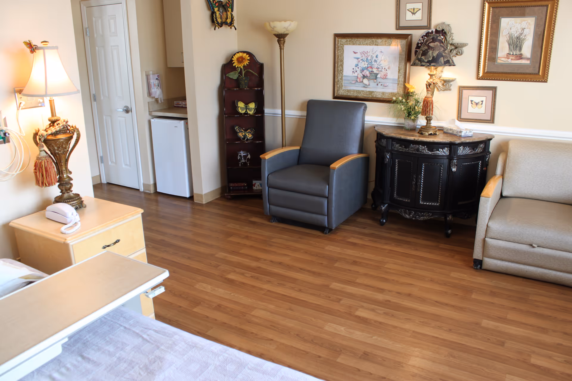 Cozy hospice patient room with bed, seating area, and decorative furnishings.