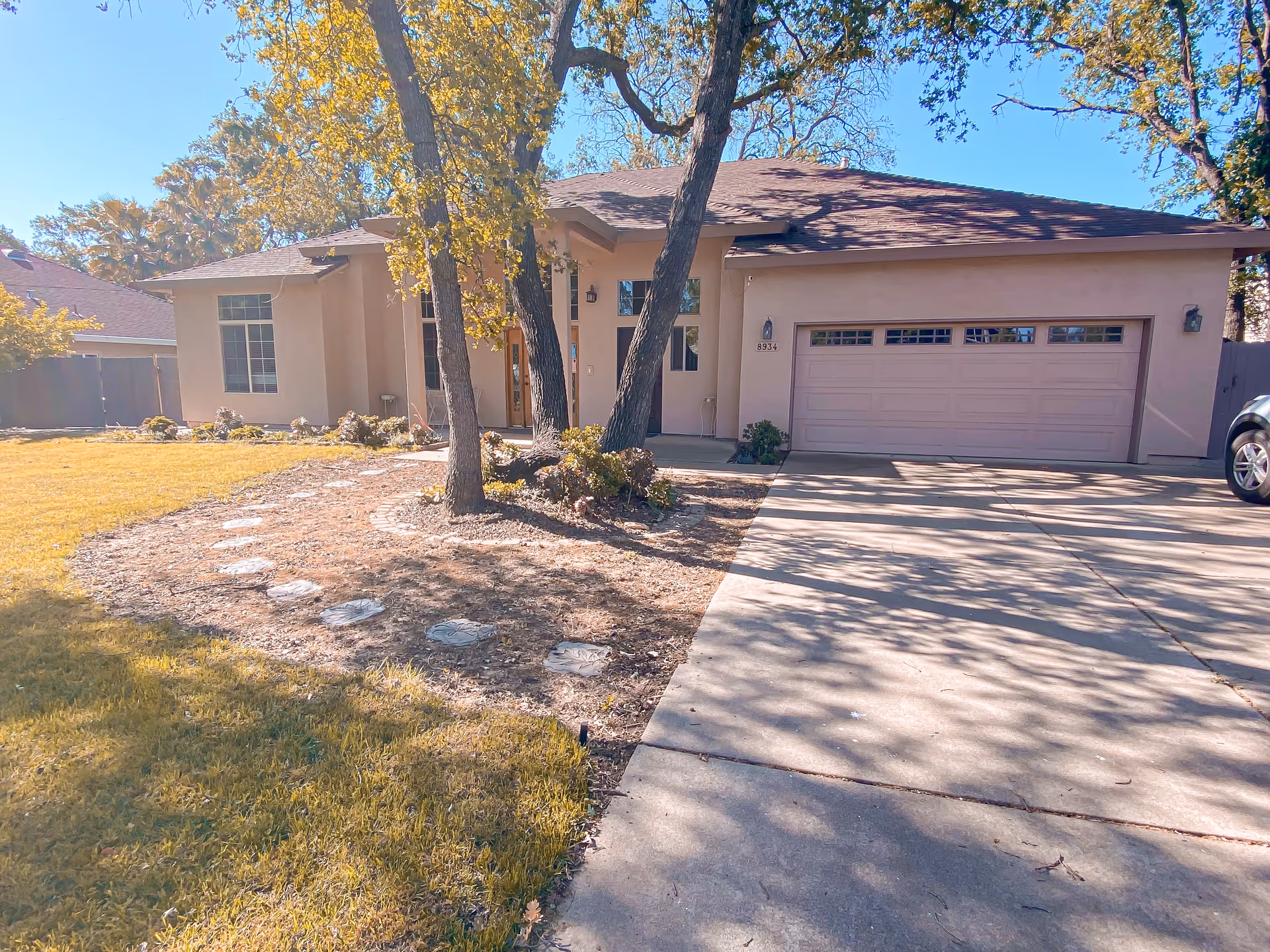 A single-family residence with a two-car garage, driveway, and trees in front yard.