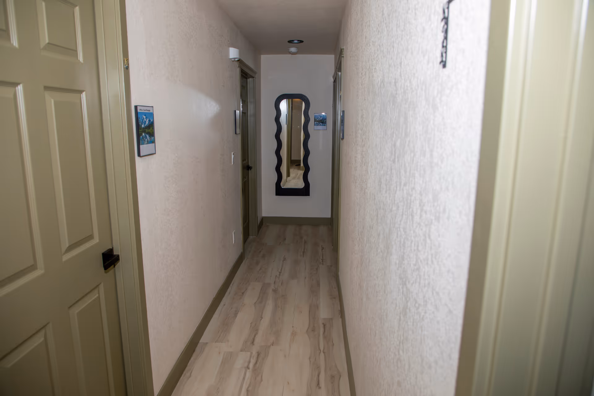 Narrow interior hallway of a senior home with doors and a decorative mirror at the end