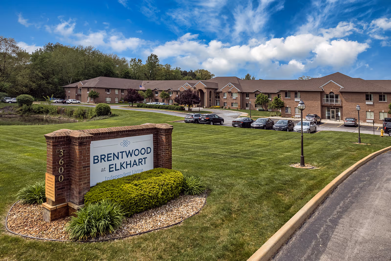 Sign and front lawn of Brentwood at Elkhart independent living facility with a brick two-story building and parking lot in the background.