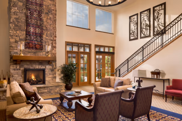 Spacious living room with a stone fireplace, comfortable seating, large windows, and a staircase.
