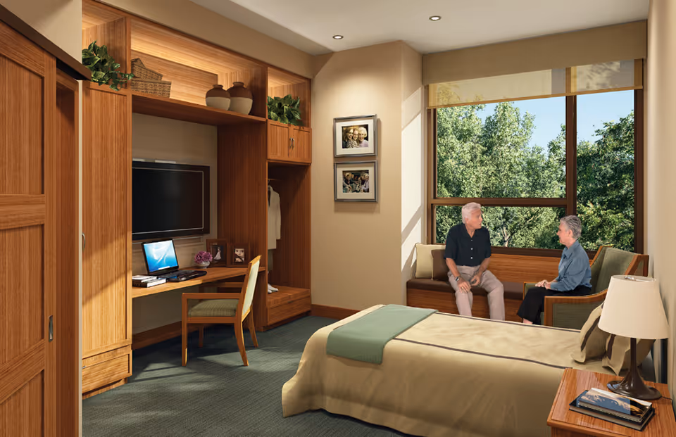 Two seniors sit on a couch beside a large window in a wood-paneled hotel-style bedroom.