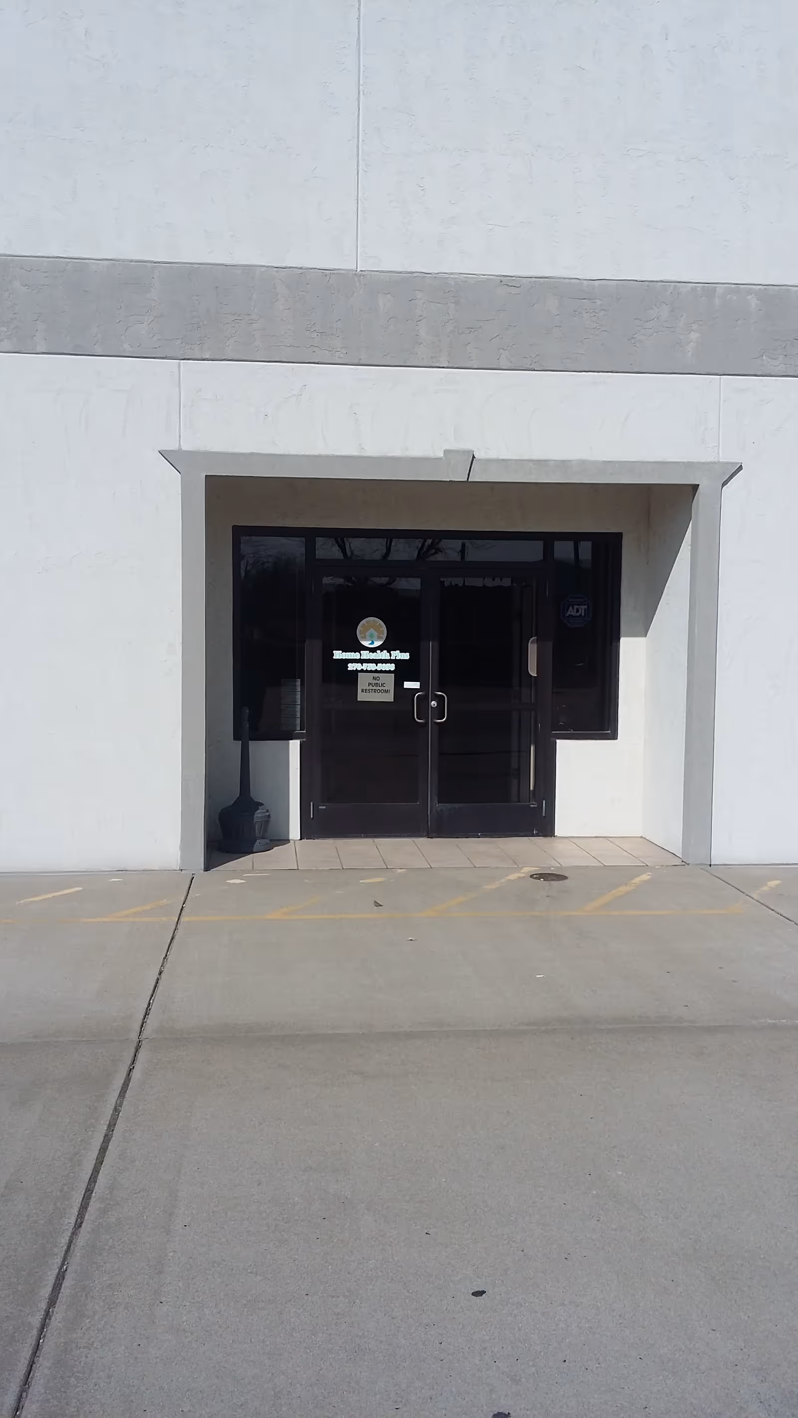 Front entrance to Home Health Plus Inc facility with glass doors and concrete exterior.
