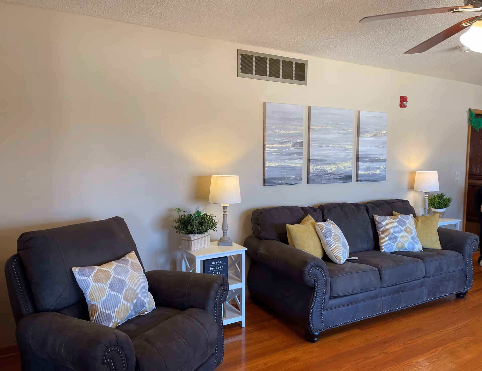 Cozy living room with two dark sofas, side tables, lamps, and wall art.