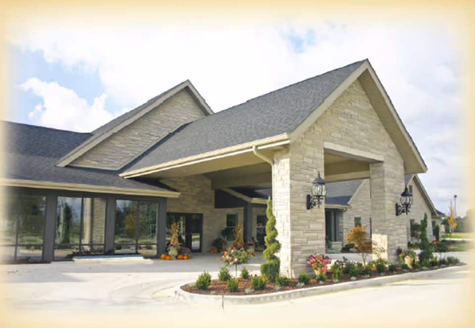 Exterior view of a senior living facility with stone facade, entrance, and landscaped grounds.