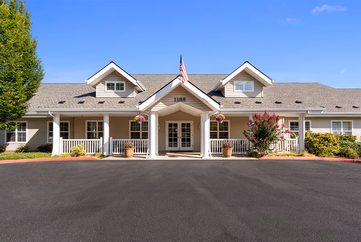 Senior living facility with a covered entrance, American flag, and potted plants.