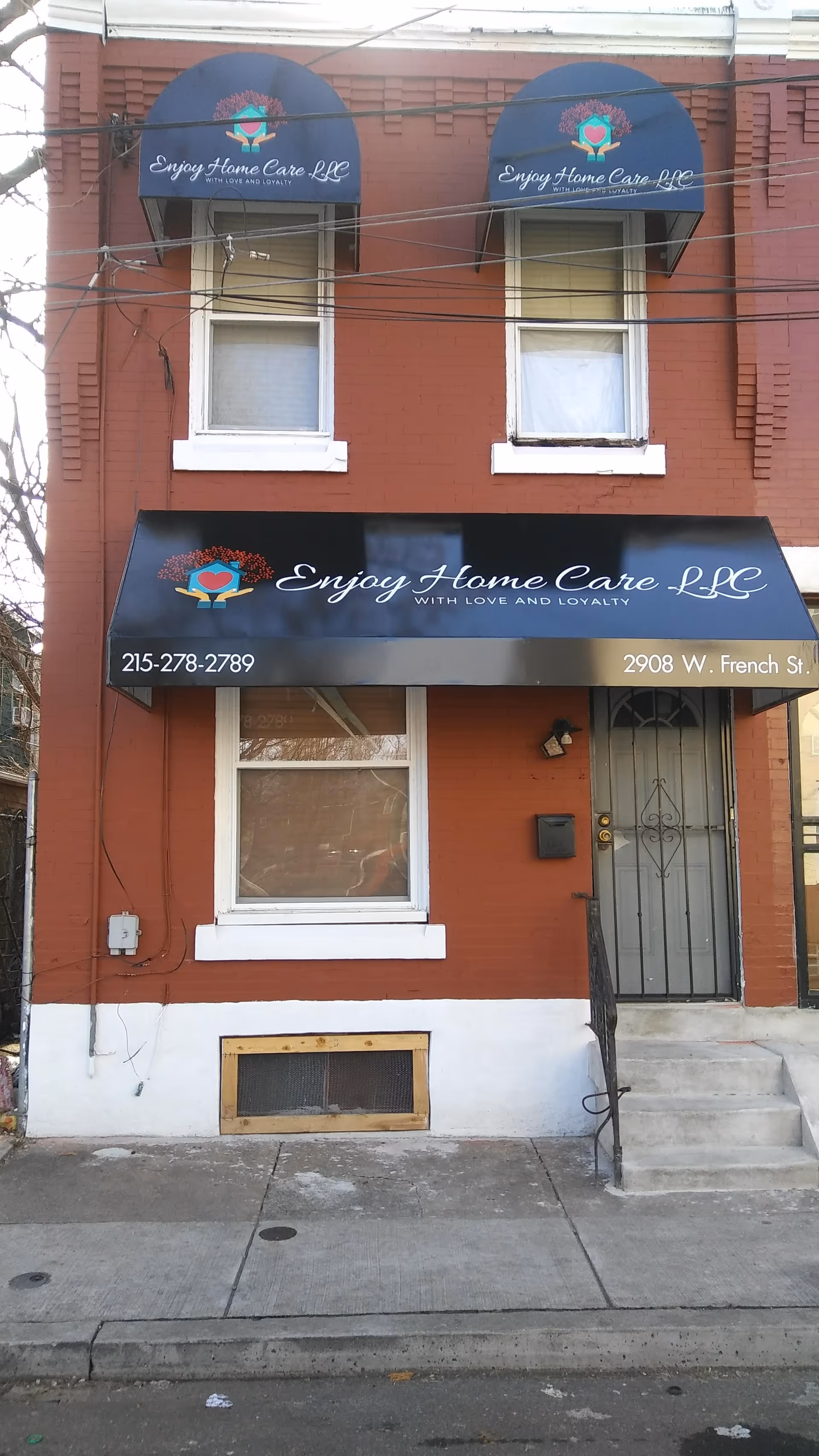 Brick building storefront with blue awnings displaying Enjoy Home Care LLC.