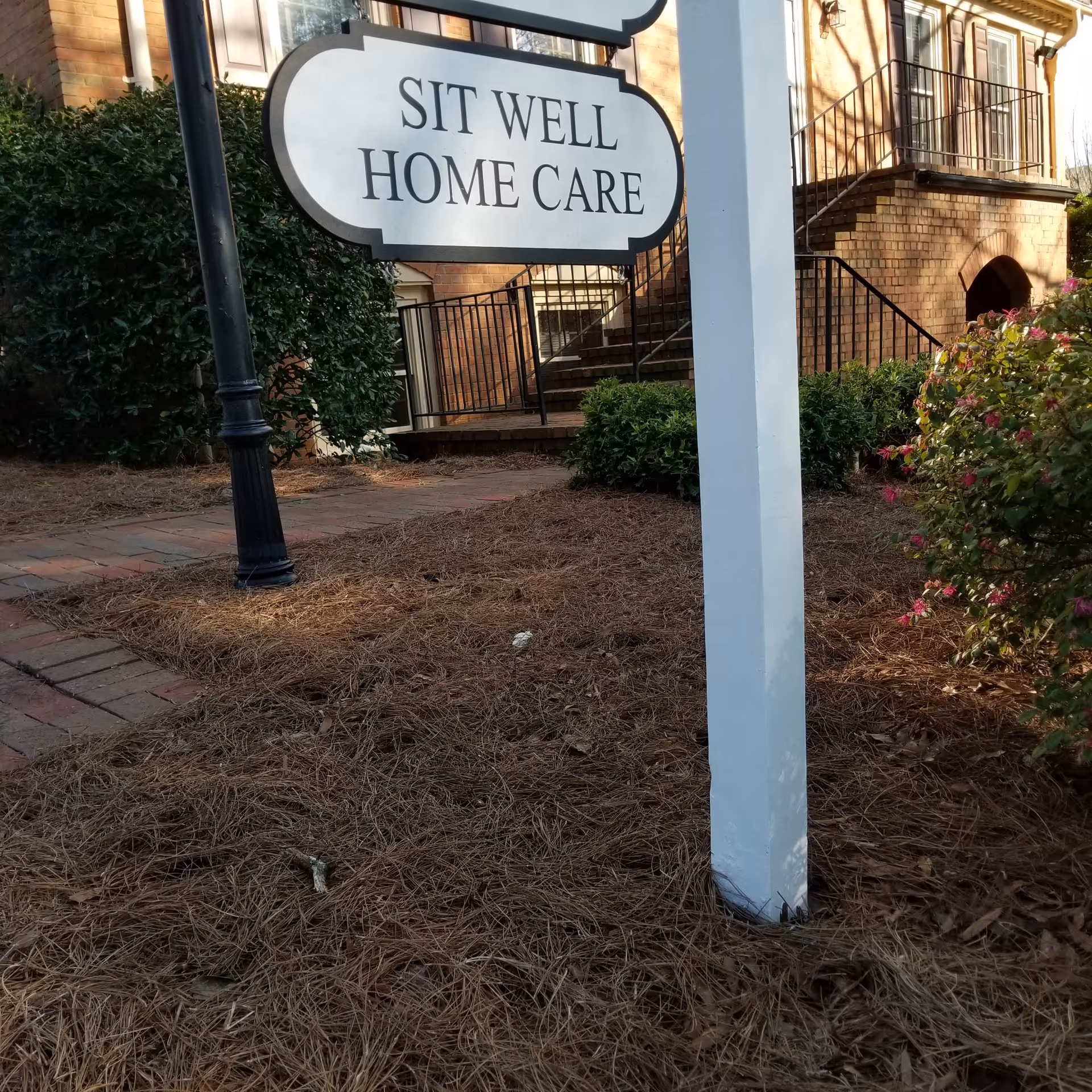 Outdoor view of Sit Well Home Care sign by the building entrance.