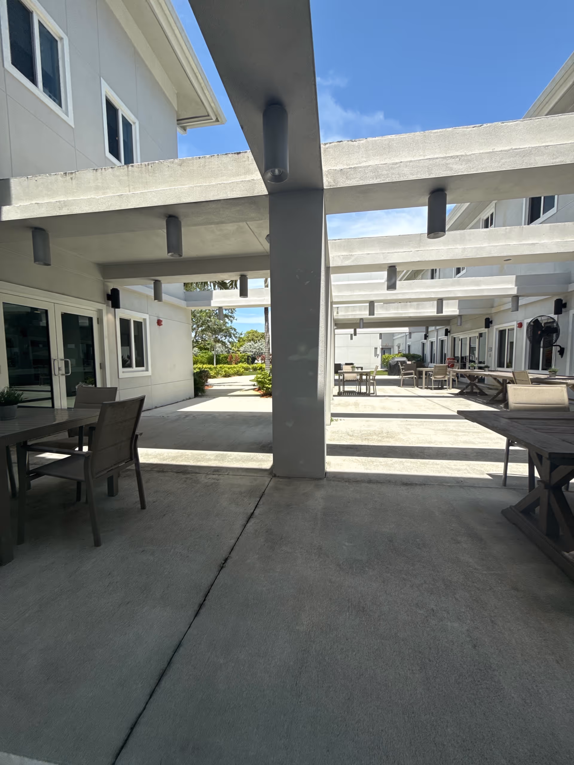 Outdoor communal patio with furniture and shaded walkways between white facility buildings.