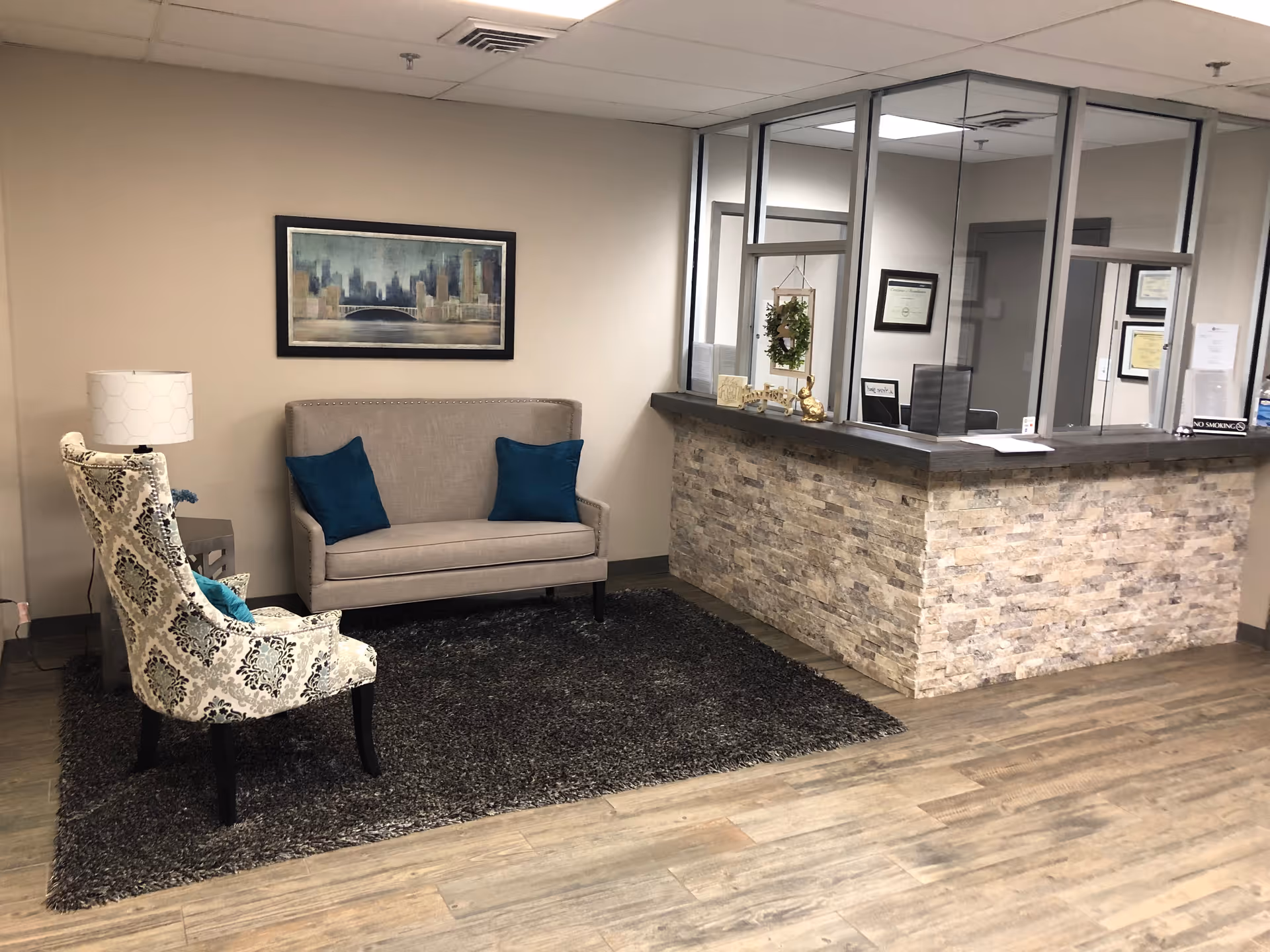Reception lobby with sofa, patterned chair, rug, wall art, and stone-front reception desk.