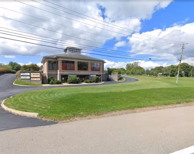 Exterior view of a two-story senior care facility with a curved driveway and green lawn.