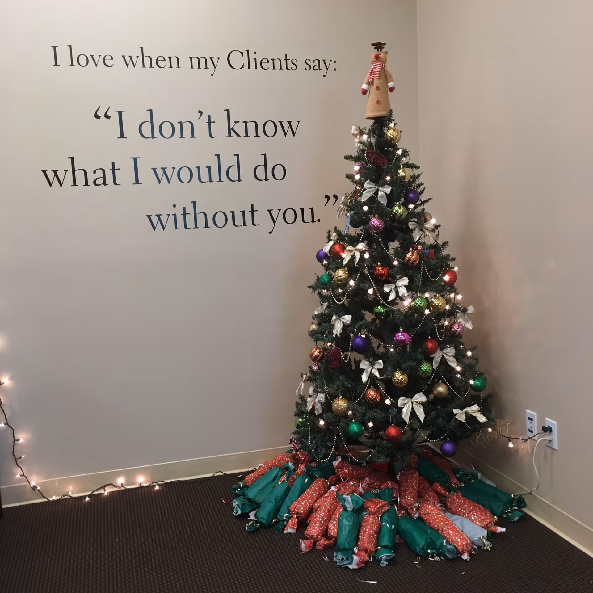 Decorated Christmas tree beside a wall with a quote and string lights.