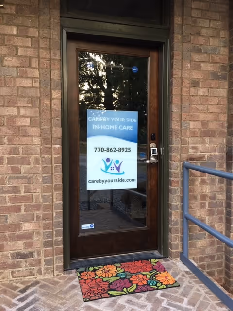 Brick exterior entrance with glass door and a colorful floral doormat.