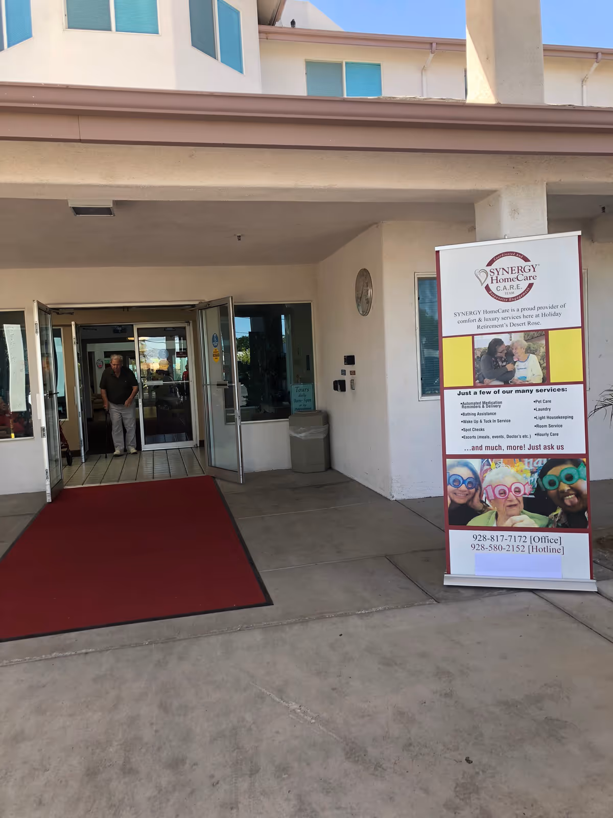 Entrance of SYNERGY HomeCare Desert Rose building with open doors and a red carpet mat.