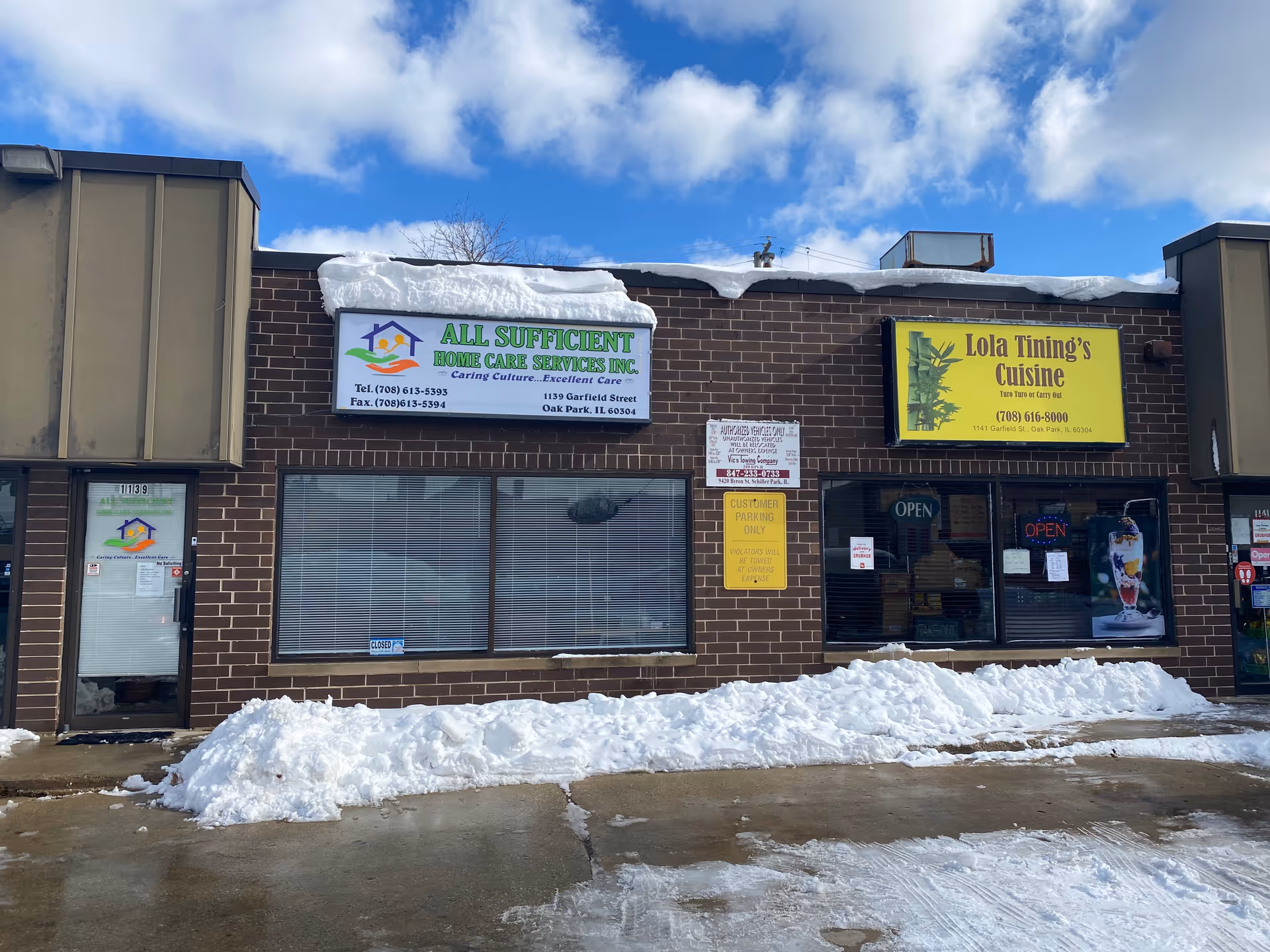 Brick storefront with two signs: All Sufficient Home Care Services and Lola Tining's Cuisine, snowy grounds.
