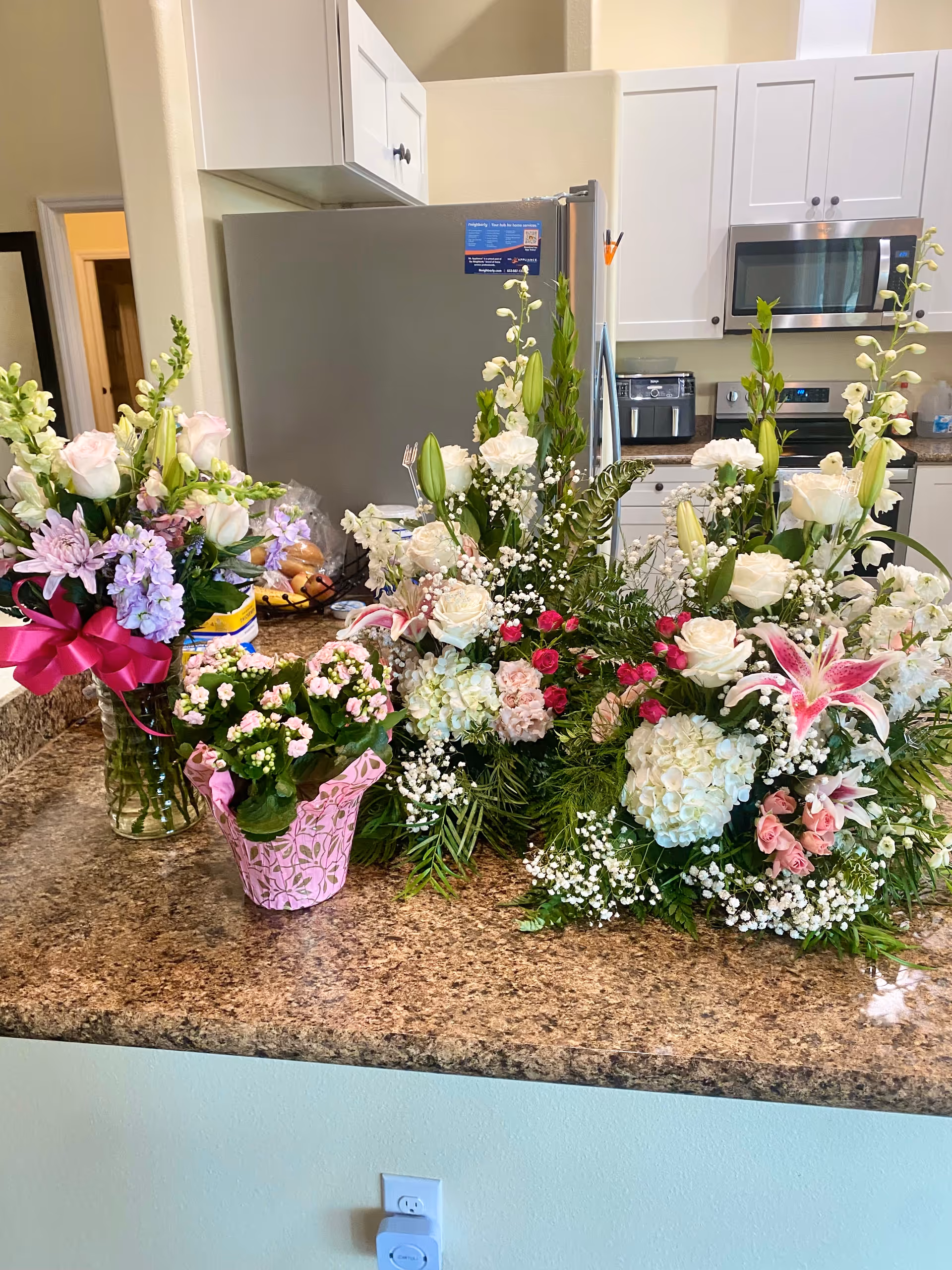 Kitchen counter with several flower bouquets beside a stainless refrigerator and white cabinets.