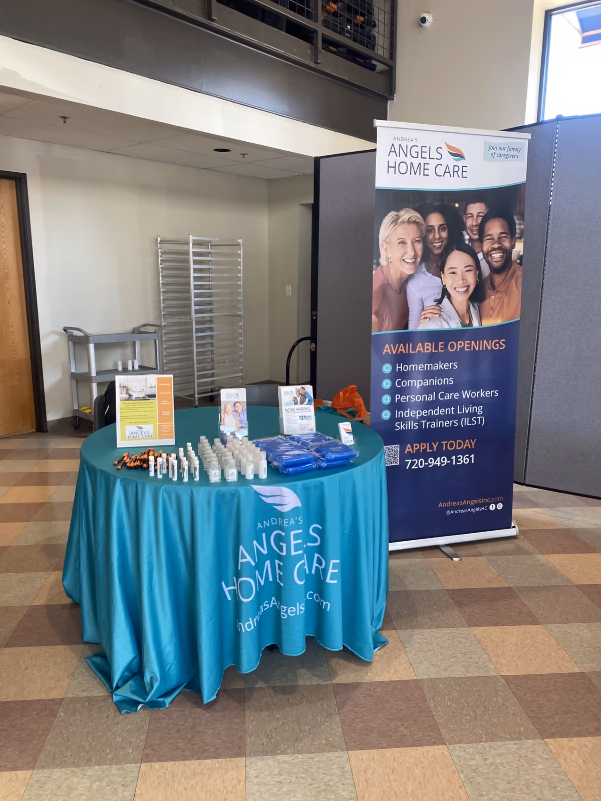 Promotional table with teal tablecloth and banner for Andrea's Angels Home Care in a lobby.