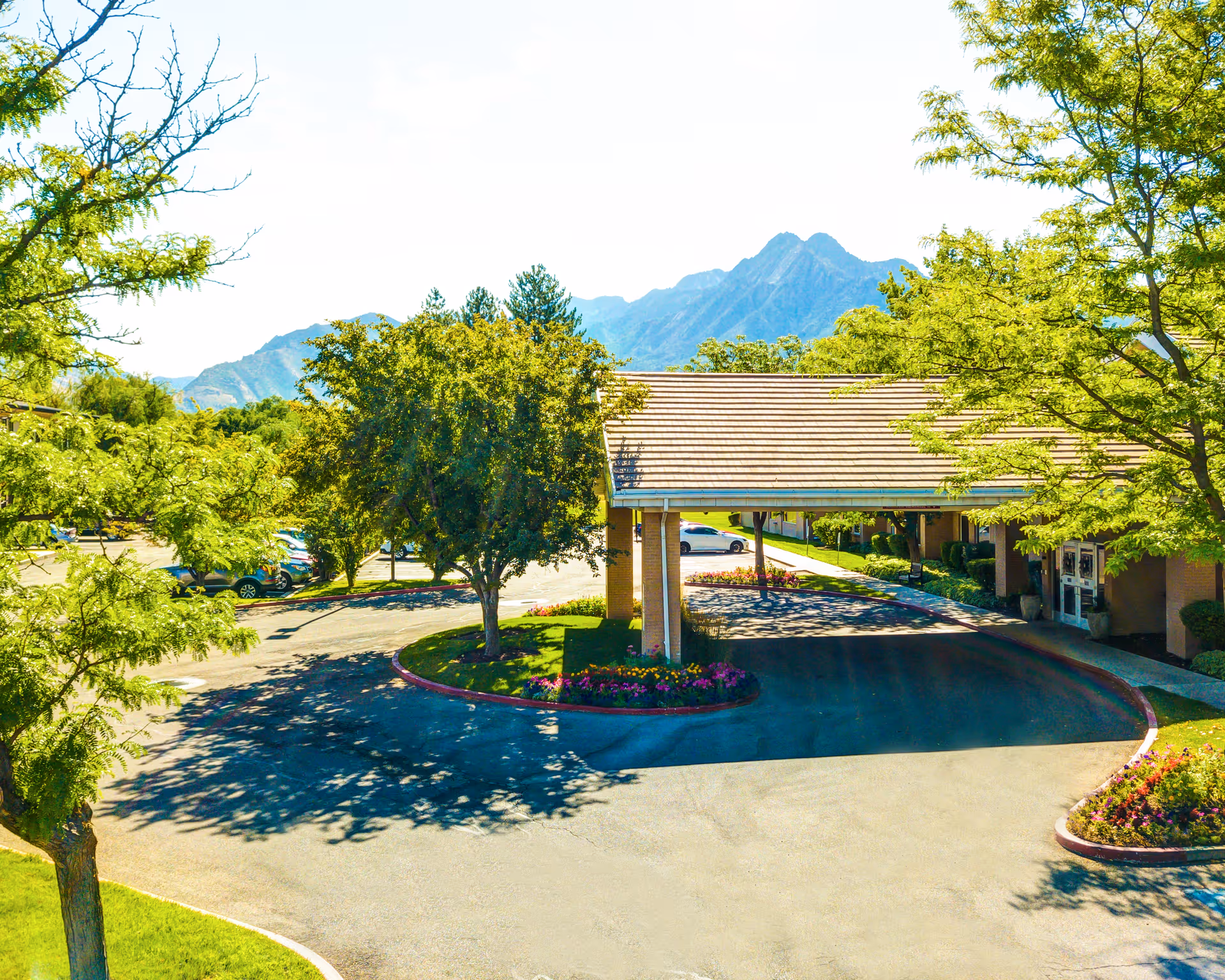 Exterior view of a senior living facility entrance with a covered driveway and mountains behind.