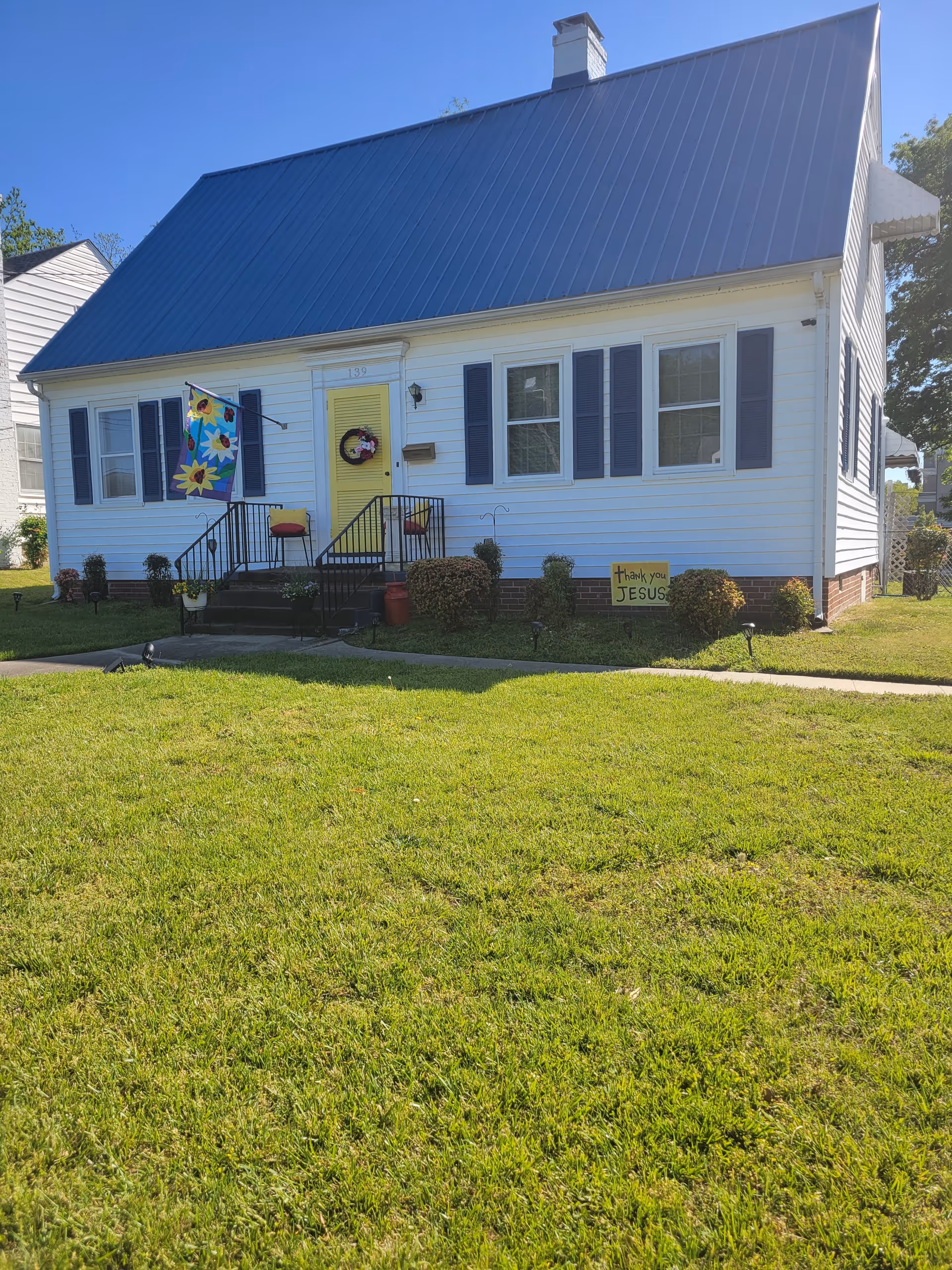 White senior living facility with a tall blue metal roof, front steps, and lawn.