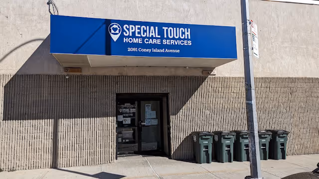 Exterior view of Special Touch Home Care Services building with a blue sign and recycling bins.
