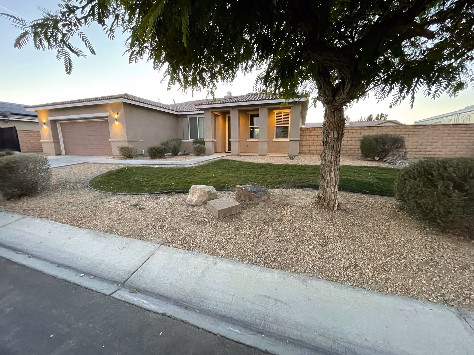 Single-story tan senior living facility front with desert landscaping, lawn, and a prominent tree.