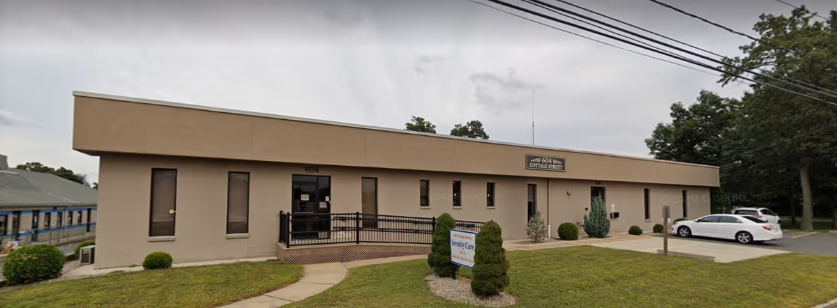 Single-story beige facility with a centered entrance, signage, landscaped front, and adjacent parking.