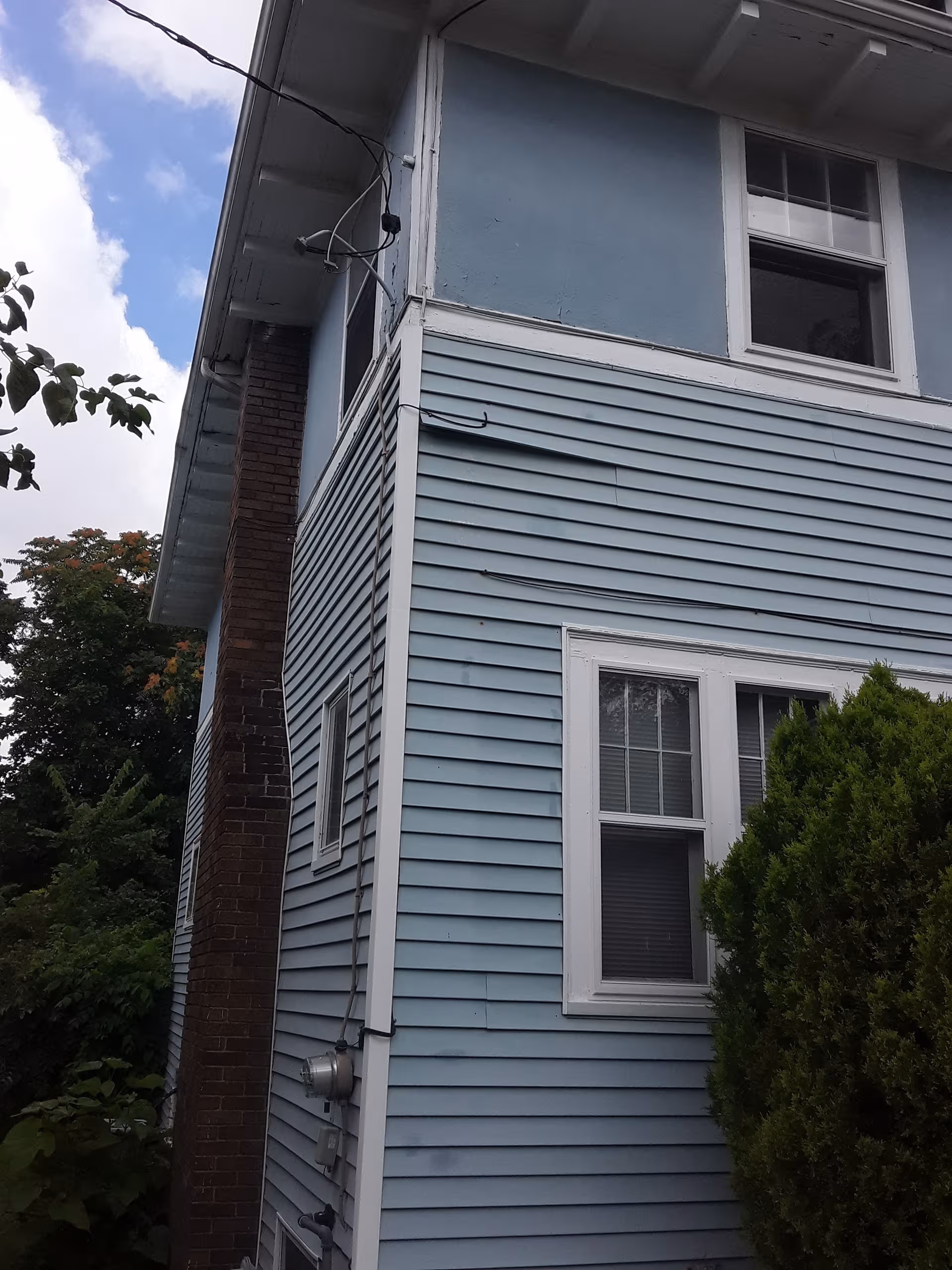 Two-story blue building exterior with white trim, windows, and a brick chimney.