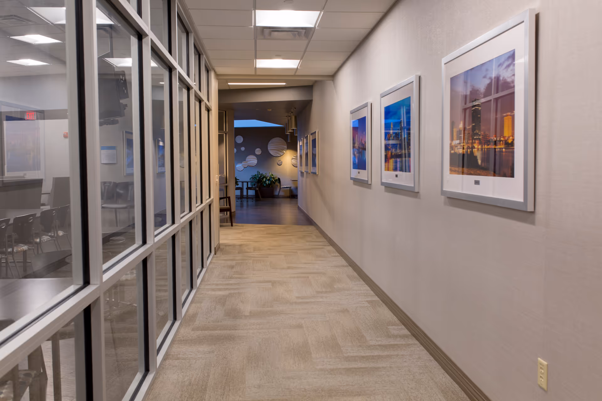 Long hallway in a senior living facility with glass walls, framed pictures, and carpet.