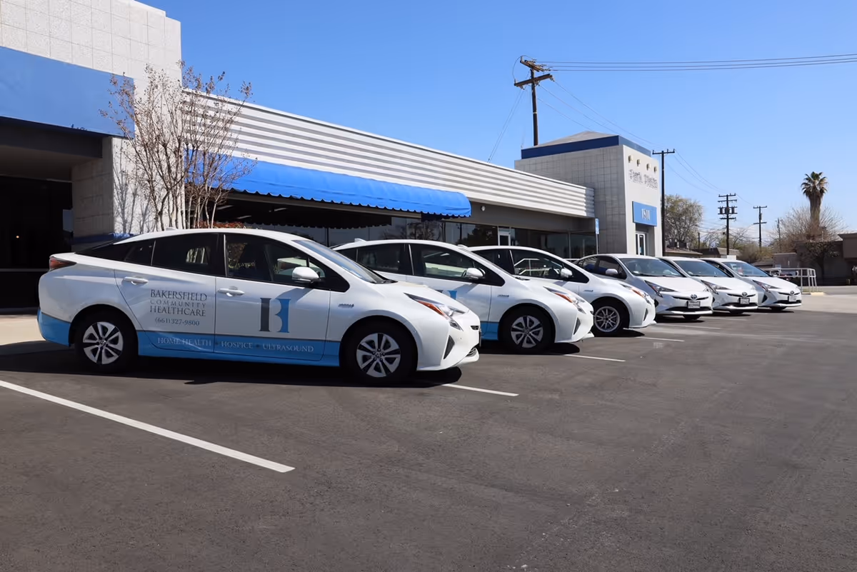 Exterior view of Bakersfield Community Hospice facility with a line of white cars in parking lot.
