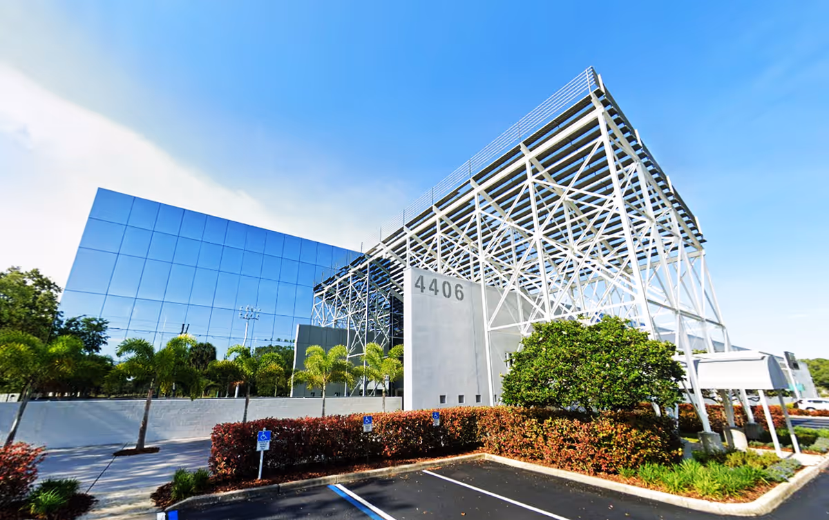 Modern exterior of a glass-fronted facility with a white lattice steel structure.
