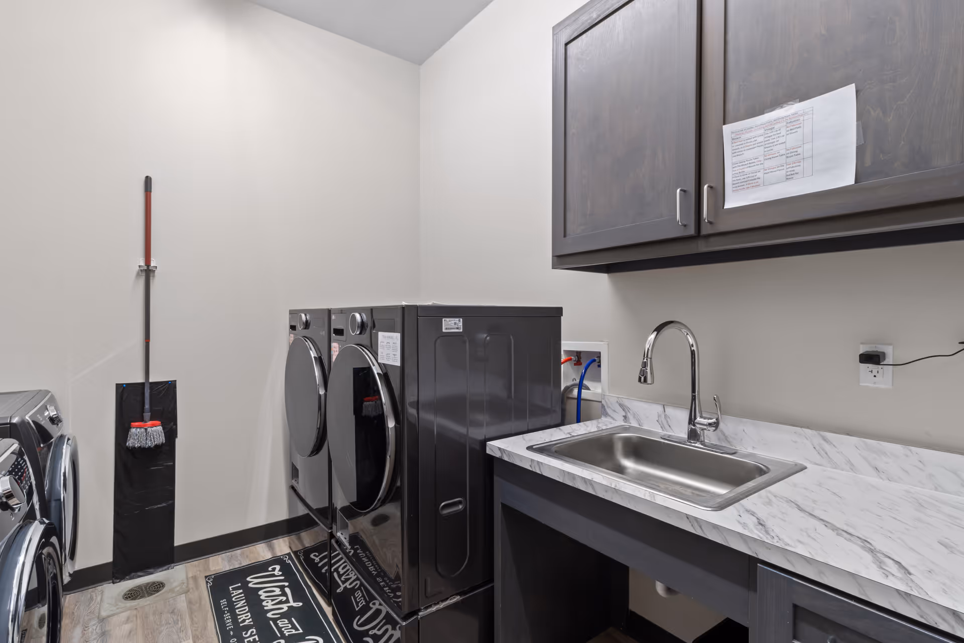 Care facility laundry room with front-load washers, a dryer, sink, and cabinets.