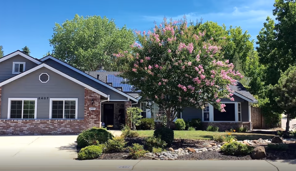 Single-story senior living facility with gray siding, brick accents, and blooming tree front yard.