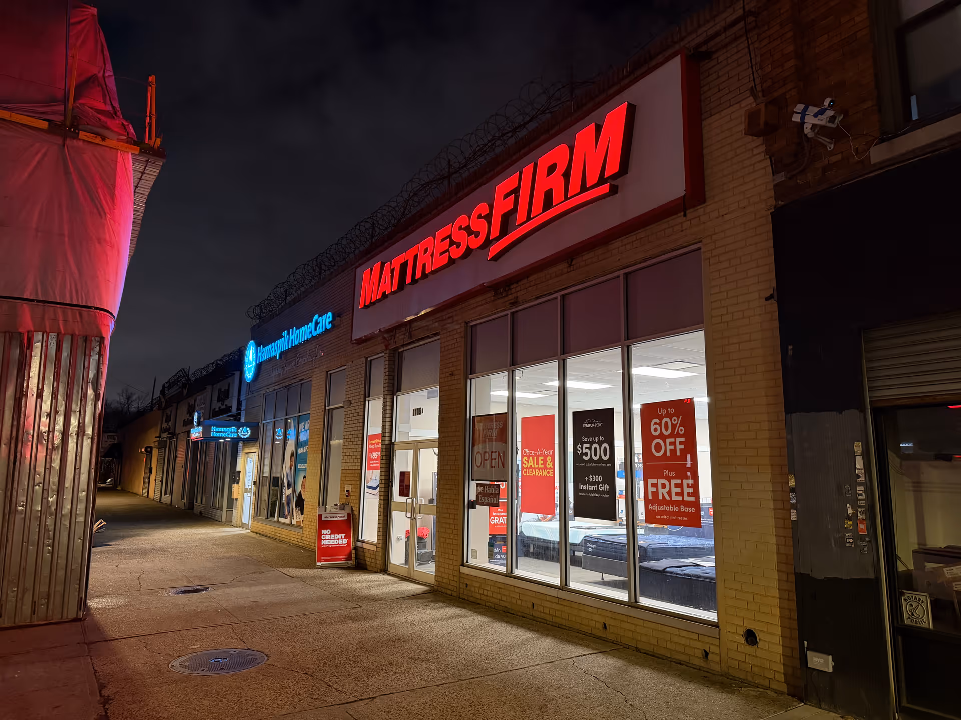 Nighttime storefront row with Hamaspik HomeCare sign beside Mattress Firm.