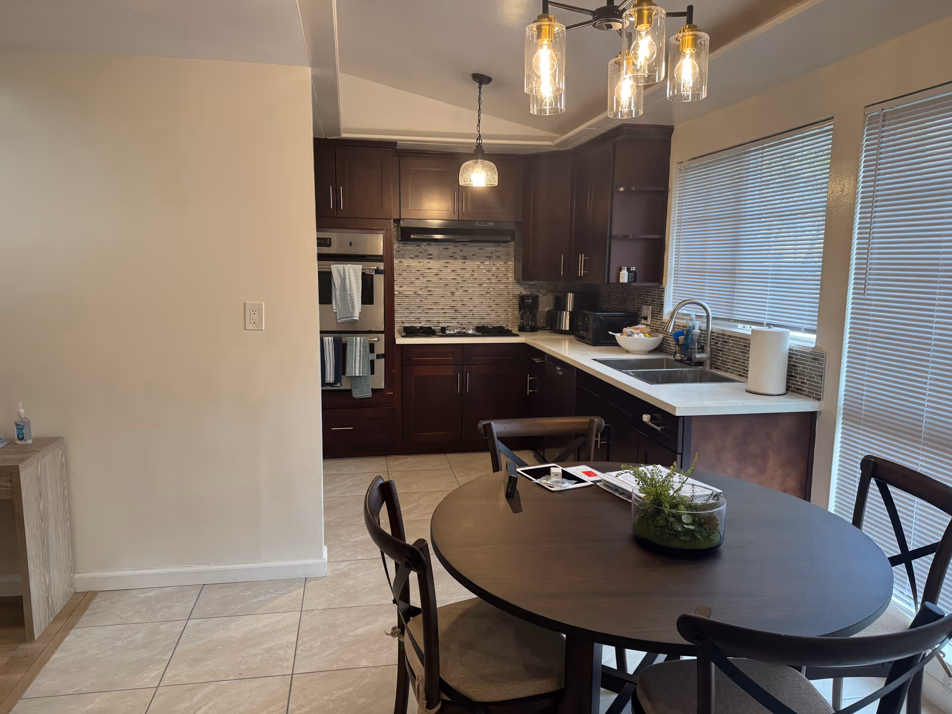 Open-plan kitchen with dark cabinets, stainless appliances, tiled floor, and a round dining table.