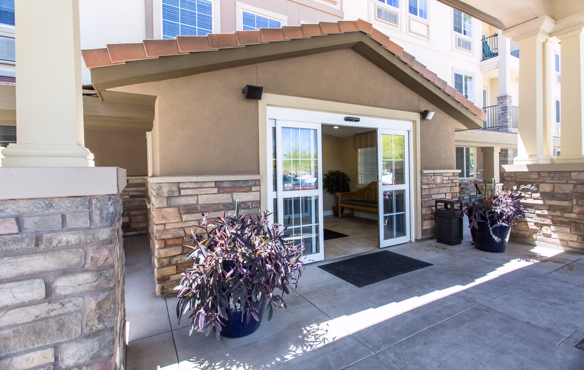 Covered entrance to Mountain Park Senior Living with glass doors, stone accents, and potted plants.