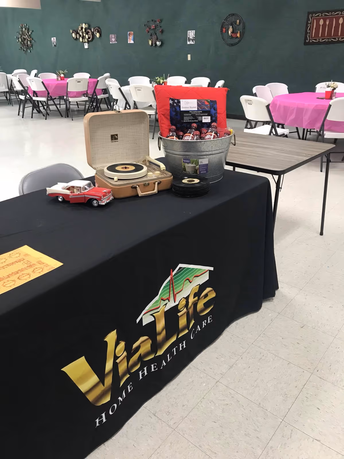 Indoor event setup with a ViaLife display table and folding chairs in the background.