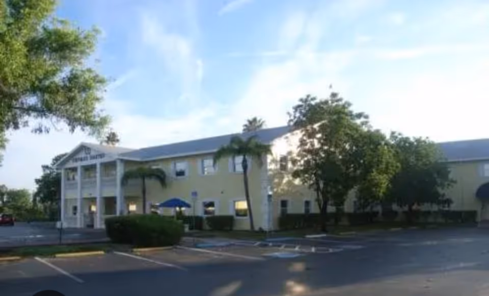 Exterior view of a two-story yellow senior living facility with parking in front